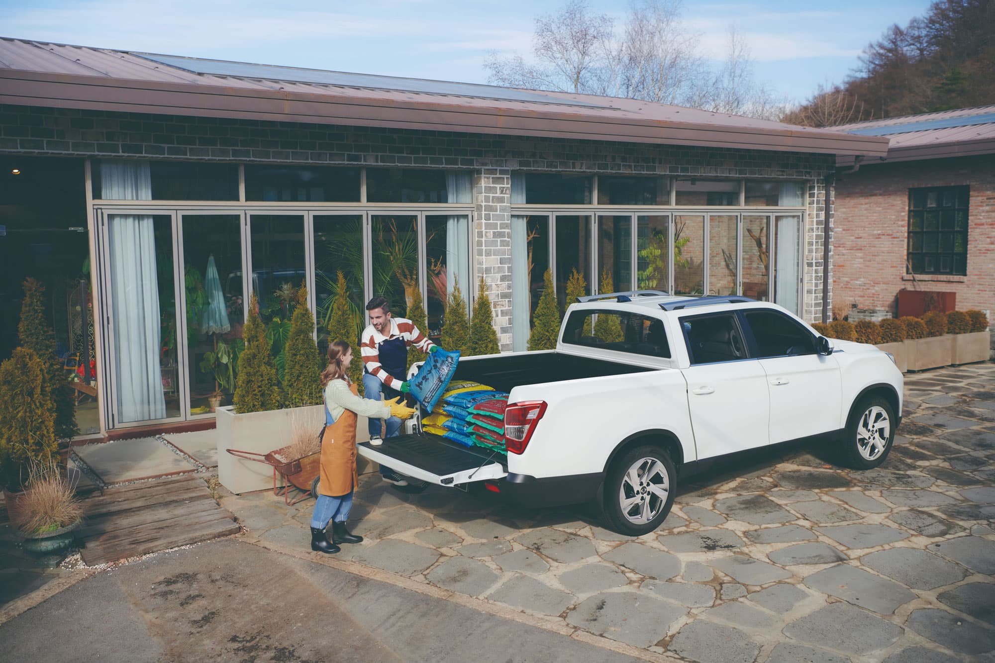 Twee mensen die de laadbak van een witte Grand Musso pick-up uitladen.